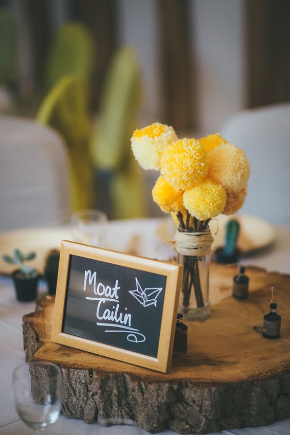 a pretty and simple wedding centerpiece of yellow pompoms, a wood slice, some candles and a chalkboard sign is wow