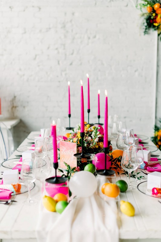 a bright wedding tablescape with hot pink candles and napkins, citrus on the table and some yellow blooms and greenery