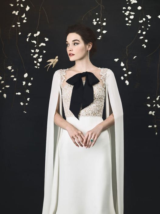 an elegant neutral wedding dress with a lace bodice, a plain skirt, a capelet, a black bow on the front for a refine dlook