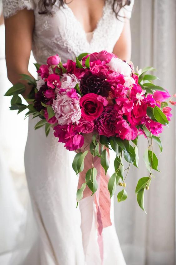 a dimensional and luxurious wedding bouquet of light pink, hot pink and purple blooms, greenery and pink ribbon is amazing