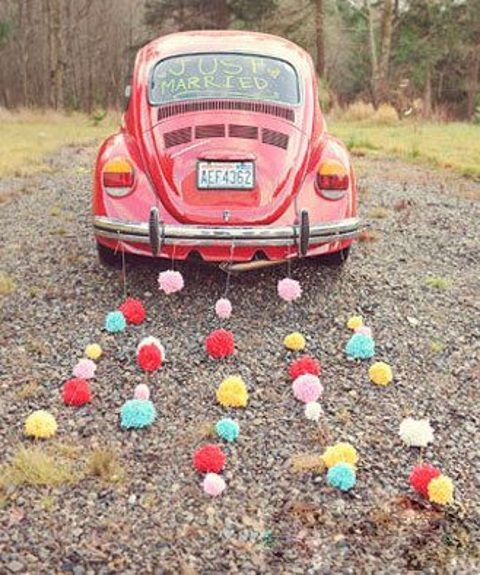 a wedding car with colorful pompom garlands instead of tin cans - much quieter and gives a unique touch to your wedding escape
