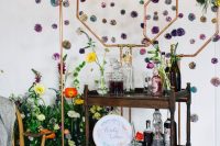 22 a wedding mini bar with hexagons and purple pompoms, bright blooms and greenery, a dark-stained cart and bold blooms and greenery