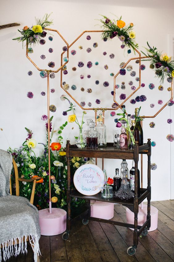 a wedding mini bar with hexagons and purple pompoms, bright blooms and greenery, a dark-stained cart and bold blooms and greenery