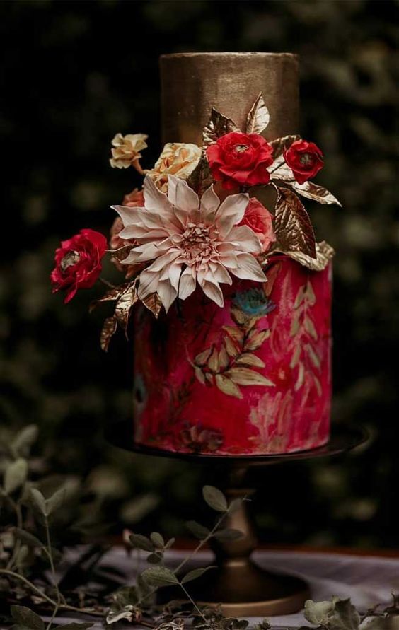 a moody and refined wedding cake with a gold and red tier, with painted gold leaves and blooms and real pink and red blooms and gold leaves for a fall wedding