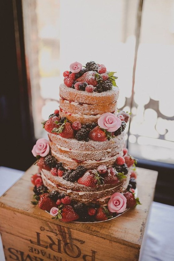 a naked wedding cake with fresh berries and pink sugar blooms is a delicious dessert for a summer rustic wedding