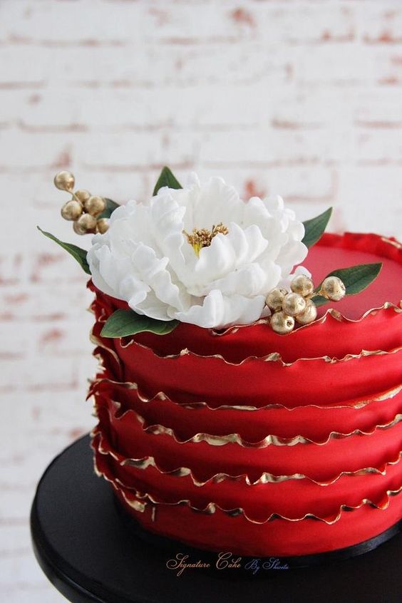 a red ruffle wedding cake with a gold rim, gold berries and a white bloom on top is a very cool and contrasting piece