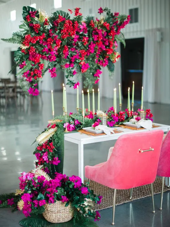 a gorgeous sweetheart table styling with red and hot pink blooms over the table, with hot pink blooms on the table and pink chairs is amazing