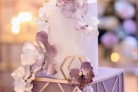 27 a sophisticated wedding cake with a square and round tiers, with purple and white blooms and gold geometric decor