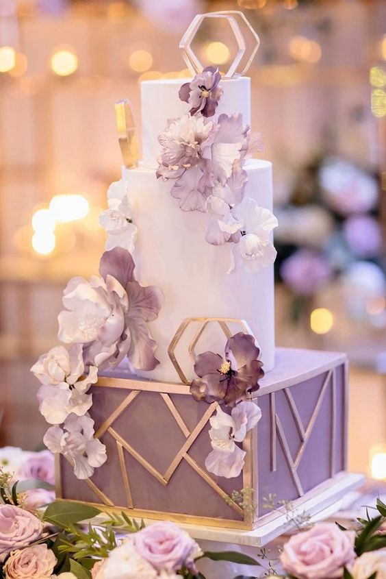 a sophisticated wedding cake with a square and round tiers, with purple and white blooms and gold geometric decor
