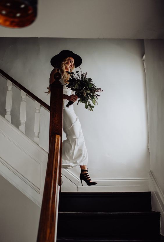 a white slip wedding dress, edgy black high top heels, a black hat and a greenery bouquet are amazing for a modern bridal look