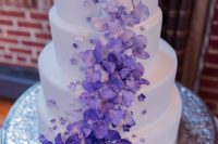 28 a white wedding cake decorated with white to deep purple blooms and smaller sugar blooms is a bold and contrasting color statement