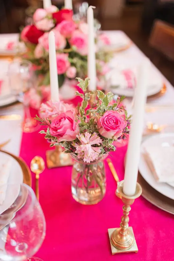 a hot pink table runner and matching hot pink blooms, candles in gold candleholders and gold chargers, gold cutlery for a glam tablescape