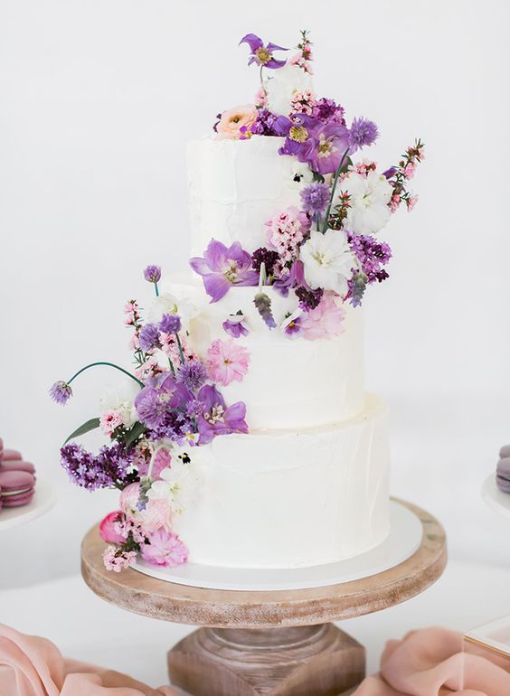 a white wedding cake that received a touch of color with white, pink and purple blooms looks lovely and such decor can be easily added or removed