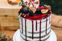 30 a semi naked wedding cake with pomegranate drip topped with fruits and greenery for a decadent fall wedding