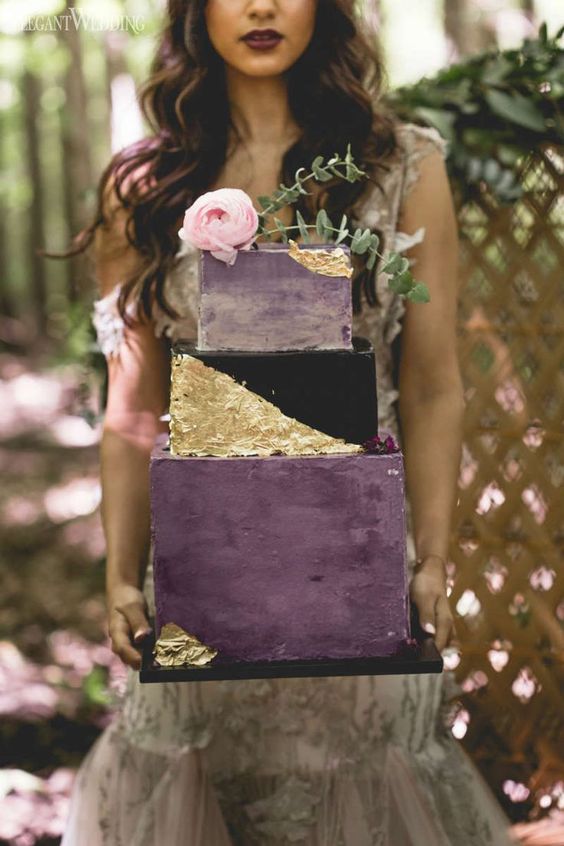 an ecnhanting square wedding cake with purple, ombre purple and black and gold tiers, with gold foil and a pink bloom on top for a witch-inspired wedding