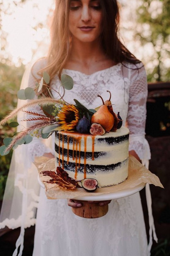 a statement fall naked wedding cake of chocolate, with pears, figs, greenery and blooms on top and some caramel drip