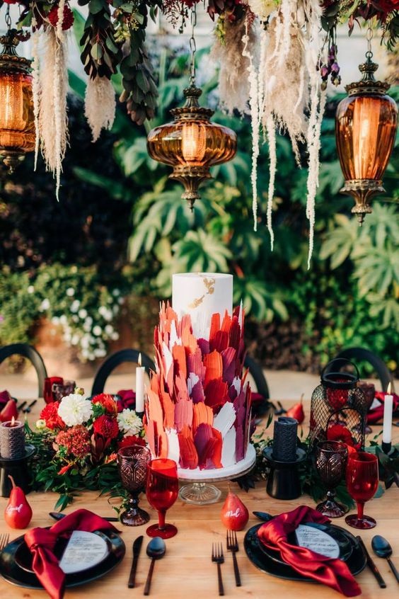 a white wedding cake decorated with white, orange, burgundy and red sugar petals is a very creative and bold idea for a modern wedding