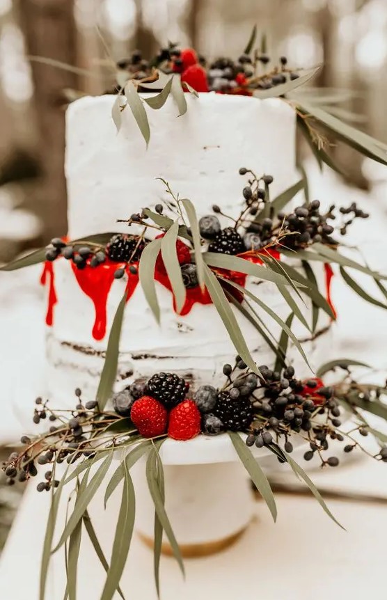 a winter wedding cake decorated with greenery, fresh berries and red drip looks very bold and spectacular