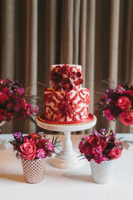 a white wedding cake with red patterns and red blooms is a very refined and chic idea for a wedding, it looks refined and bold