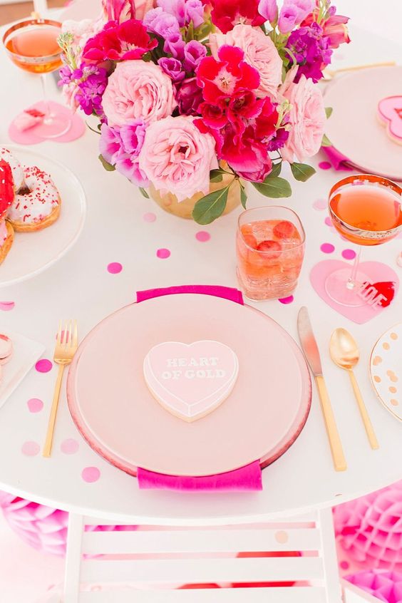 a super bright Valentine's Day wedding tablescape with polka dots, pink porcelain and hot pink napkins, a light pink and hot pink floral centerpiece and gold cutlery