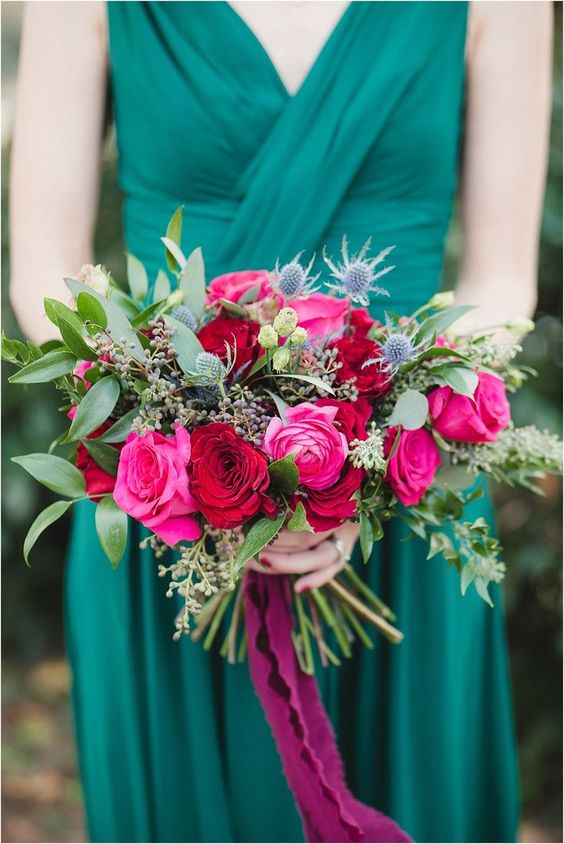 an emerald draped bridesmaid dress and a jewel-tone bouquet with hot pink, red blooms, greenery and thistles for a colorful fall wedding