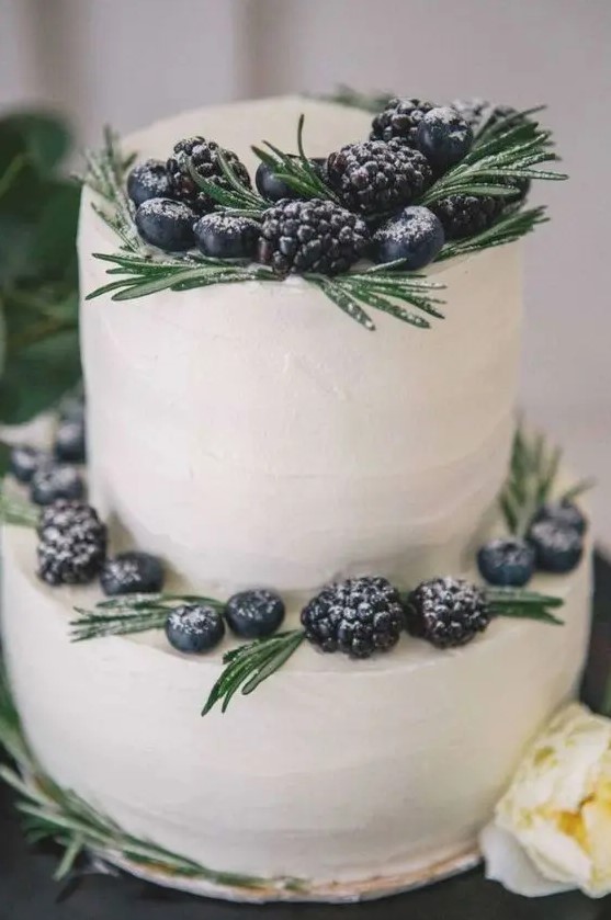 a simple white buttercream wedding cake decorated with rosemary and fresh berries is a stylish idea for a winter wedding