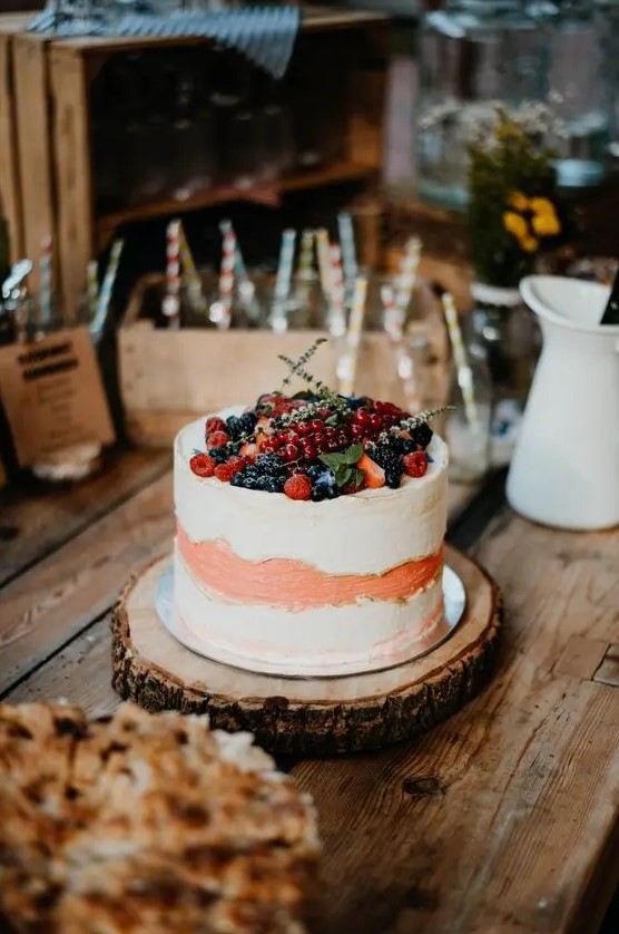 a white and peachy buttercream wedding cake topped with fresh berries and greenery is a lovely wedding dessert