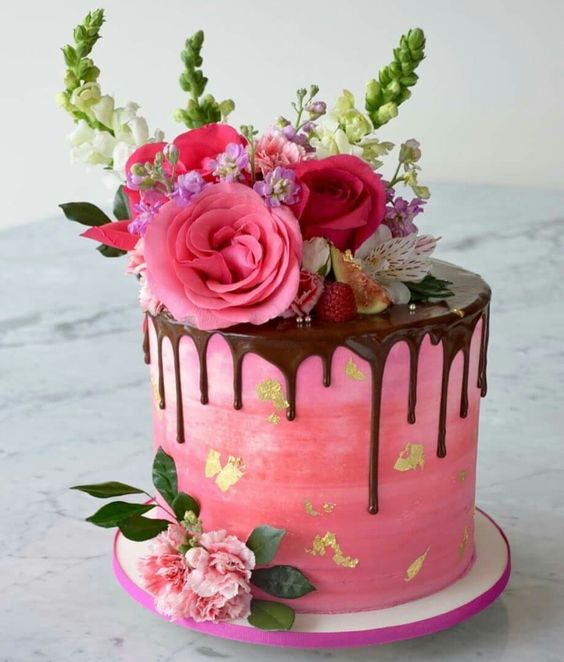 an ombre pink wedding cake with gold leaf, chocolate drip, hot pink and light pink blooms, greenery and berries