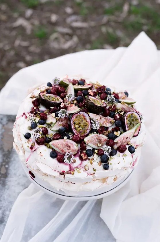a catchy pavlova wedding cake topped with fresh fruits and berries, some blooms and nuts is fantastic
