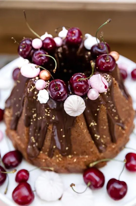 a chocolate bundt wedding cake with chocolate drip, gold leaf, fresh cherries, meringues and beads is a lovely and glam idea