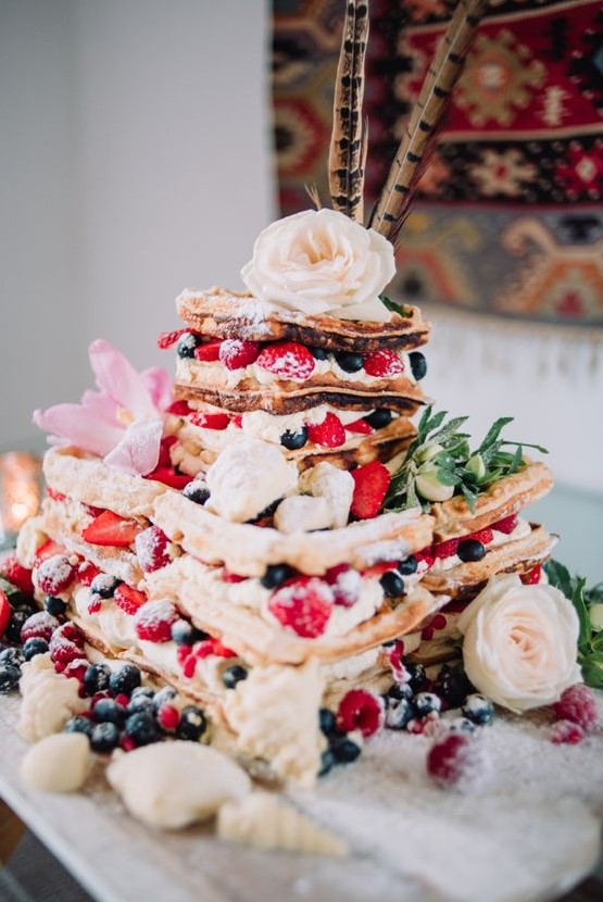 a gorgeous summer boho wedding cake with fresh berries, pink and white blooms, greenery and feathers on top