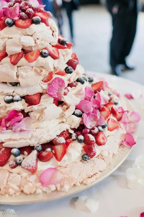 an oversized meringue wedding cake topped with fresh berries, pink petals and sugar powder is a gorgeous wedding dessert