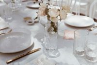 a beautiful modern wedding table setting with neutral and blush blooms, white linens and gold cutlery, elegant glasses is chic