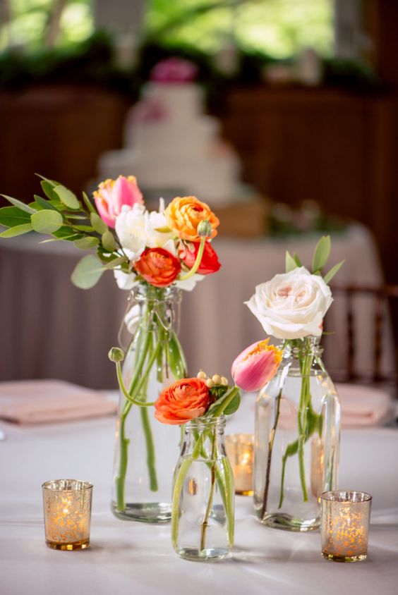 a bright cluster wedding centerpiece of bottles, blush, pink and orange blooms, candles around the bottles is a gorgeous idea