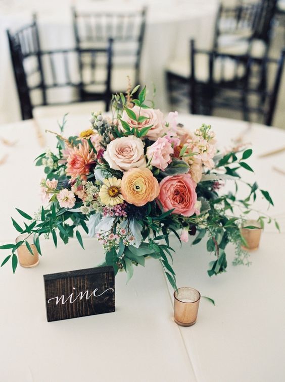 a bright wedding centerpiece of blush roses, pink and yellow ranunculus, orange dahlias, waxflower and greenery plus candles around