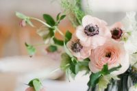 a chic wedding centerpiece of a glass vase with black framing, peachy pink ranunculus and anemones, greenery and mauve blooms is wow