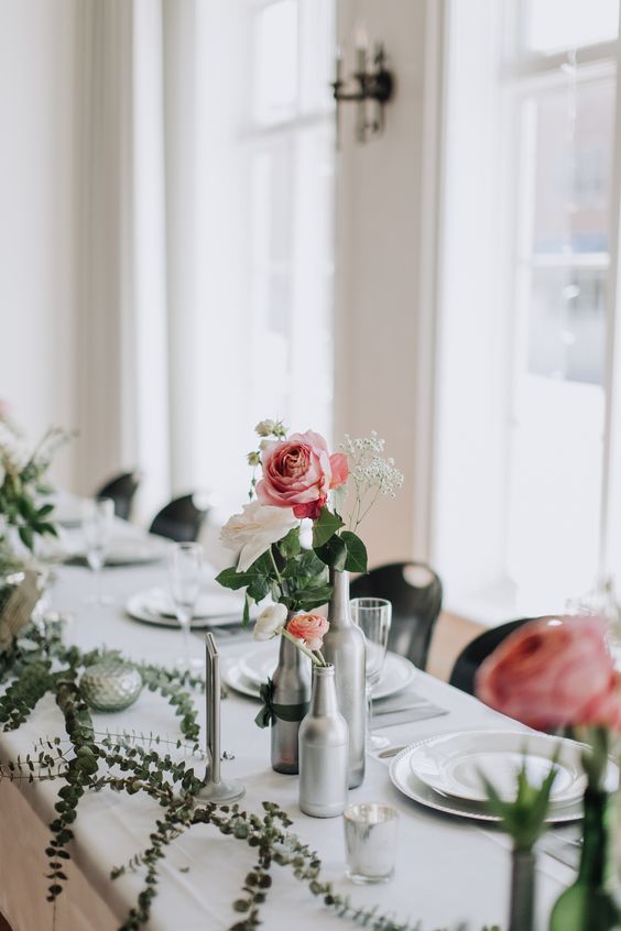 a cluster wedding centerpiece of silver bottles, white and orange ranunculus, a pink rose and some baby's breath is amazing for a relaxed wedding