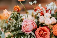 a colorful wedding centerpiece of pink and blush roses, orange ranunculus, greenery and some neutral fillers is cool for summer or fall