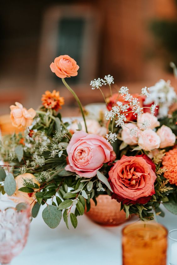 a colorful wedding centerpiece of pink and blush roses, orange ranunculus, greenery and some neutral fillers is cool for summer or fall