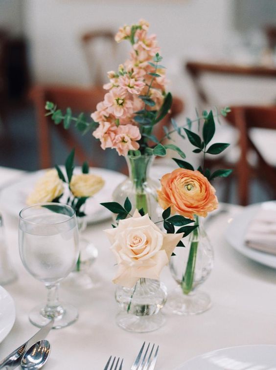 a delicate earthy-toned wedding centerpiece of a blush rose, an orange ranunculus and some pink blooms and greenery is amazing