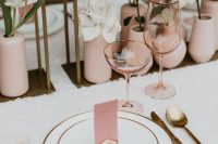 a lovely modern wedding tablescape with a neutral tablecloth, blush vases with a single bloom in each, gold-rimmed plates and gold cutlery