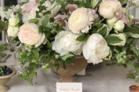 a lush and chic pastel wedding centerpiece with blush ranunculus, peony roses, greenery and berries is a fantastic idea for a garden wedding