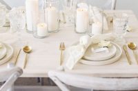 a modern neutral wedding table setting with white pillar candles, neutral porcelain and napkins, gold cutlery is amazing