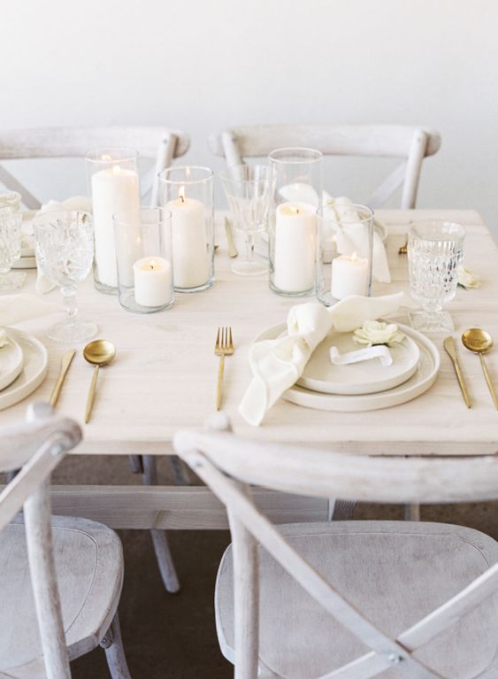 a modern neutral wedding table setting with white pillar candles, neutral porcelain and napkins, gold cutlery is amazing