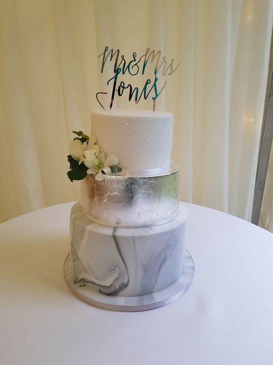 a modern wedding cake with a white glitter, silver leaf and marble tier, with white blooms and a calligraphy topper is a stunning idea