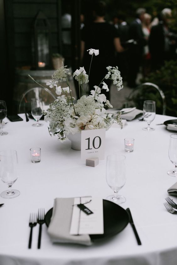 a monochromatic modern wedding tablescape with white blooms, black chargers and cutlery, candles and grey napkins