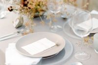 a neutral sophisticated wedding tablescape with a grey tablecloth and white napkins, clear and grey plates and bold blooms