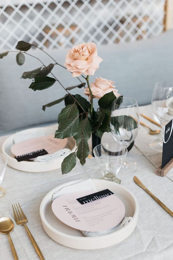 a pretty and delicate modern wedding tablescape with blush roses and blush menus, white porcelain, gold cutlery and black touches