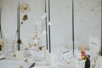 a pretty modern wedding tablescape with tall and thin black candles, a bit of dried blooms, white linens and plates is amazing