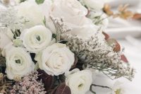 a refined and chic contrasting wedding centerpiece with white roses, ranunculus, dark foliage and waxflower is a lovely idea to rock